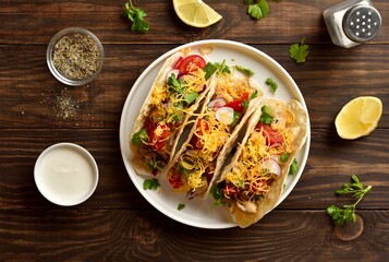 Tacos with vegetables, chicken meat and cheddar cheese over wooden background