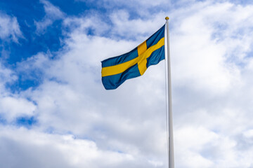 Swedish flag against blue sky white clouds. Swedish flag fluttering on wind. Sveriges nationaldag. National Day of Sweden. Swedish Flag Day