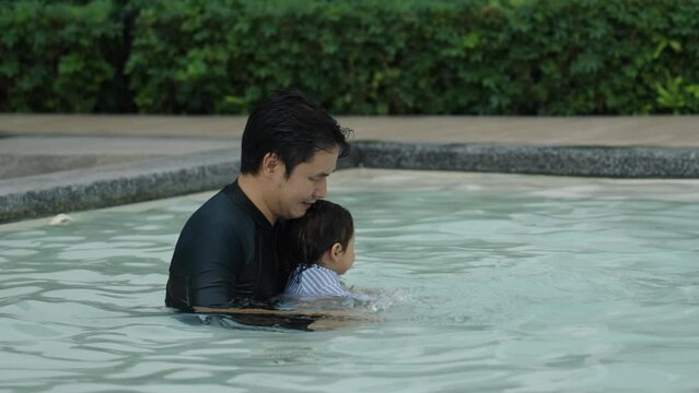 happy father with todler baby playing water splashing in a swimming pool