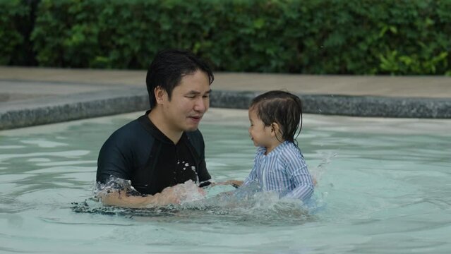 happy father with todler baby playing water splashing in a swimming pool