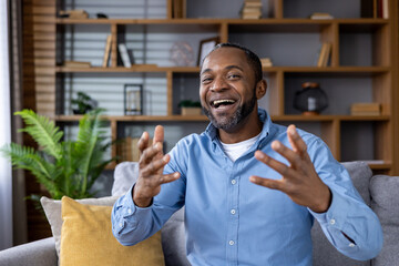 Happy man smiling and gesturing during video call sitting on sofa. Engaging in lively conversation...