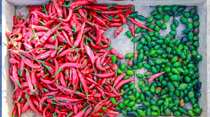 A wooden crate overflowing with red and green chili peppers, a vibrant display of spices. A colorful display mix of red and green peppers at a local market