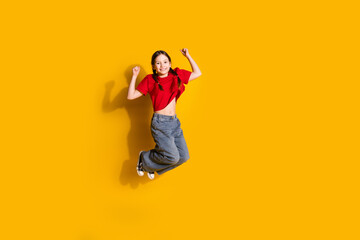 Full size photo of lovely small girl jump raise fists wear t-shirt isolated on yellow color...