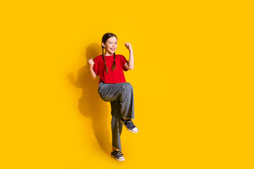 Full size photo of lovely small girl raise fists empty space wear t-shirt isolated on yellow color background