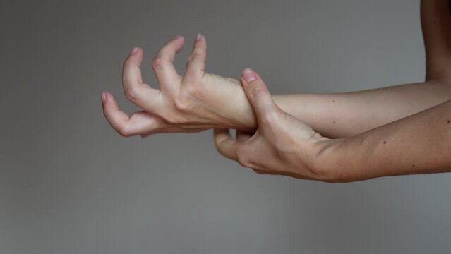 Cropped shot of a young woman holding a wrist in her hand on a grey background. Wrist injuries, arm pain, carpal tunnel syndrome, neuralgia. Dislocated wrist. Medical concept