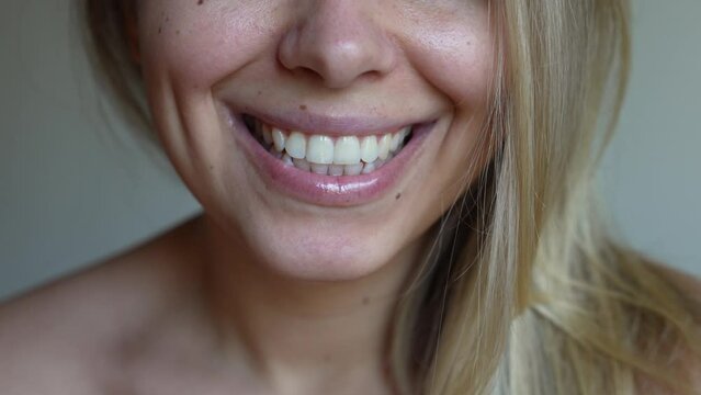 Cropped shot of a young smiling caucasian blonde woman with perfect white even teeth on a grey background. Oral hygiene, dental health care. Teeth whitening. Dentistry, beautiful smile