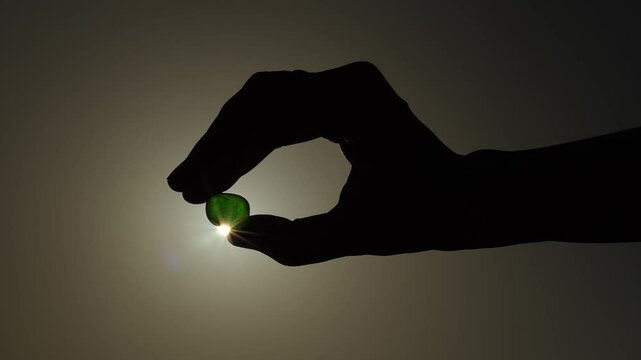Hand holds a transparent stone in backlight