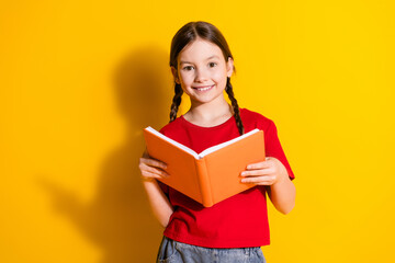Photo of lovely small girl read book wear t-shirt isolated on yellow color background