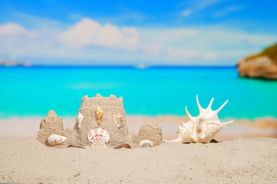 Sand castle and sea shell on sand beach at tropical resort. Family vacation. Relax on the beautiful sea coast beach. Azure water on the ocean, sea coast resort. Summer holidays. Blue sky. Copy space.