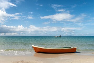 Orange boat on the shore with boat in the background