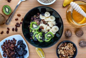 Healthy breakfast. Soaked organic raw barley, walnuts, kiwi, banana, raisins, prunes and honey on the table, wooden background