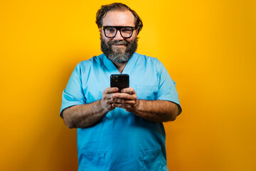 Doctor in blue coat on yellow background using a smartphone.