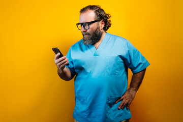 Doctor in blue coat on yellow background using a smartphone.