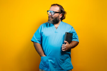 Doctor in a blue coat on a yellow background and a tablet under his arm. Concept of use of...