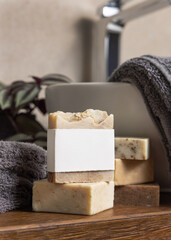 Soap bar with blank label near grey towels, plant and vessel basin on wood in bathroom, mockup