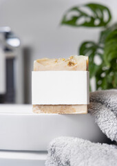 Soap bar with blank label on vessel sink near grey towels and plant close up, mockup