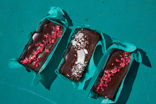 Three chocolate bars with dried fruit toppings on teal rustic surface