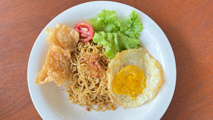Fried noodle (mie goreng) with vegetables, instant noodles with sunny side up eggs. Indonesian cuisine street food. Indomie one of famous food from indonesia