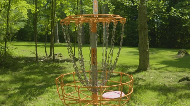 A close-up of a disc golf basket as the disc enters, highlighting the target of the game in a wooded park