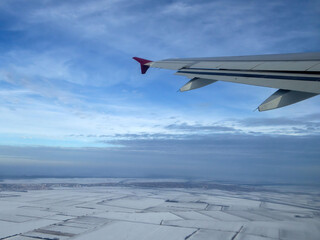 View of wing from plane window, flying above snowy fields in winter