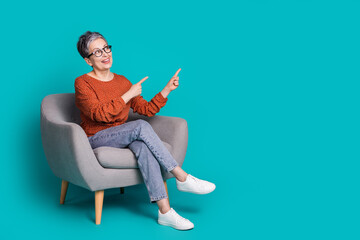 Full length photo of lovely pensioner lady sit armchair look point empty space dressed brown garment isolated on cyan color background