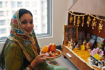Portrait of Indian woman in scarf looking at camera while making offerings near the altar