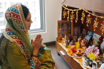 Indian woman in scarf sitting with her eyes closed and praying at altar in the room