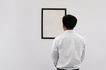 Man looking poster on wall. Man watching photo frame painting at artwork museum. Picture frames...