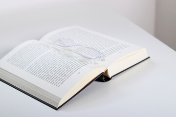 Obraz premium Close up of transparent glasses and an open book on white table 