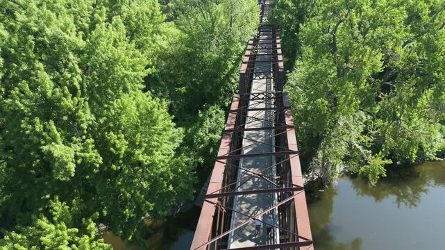 People Walking On Northampton Lattice Truss Bridge Through Foliage In Northampton, Massachusetts. aerial shot