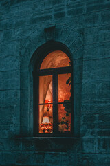 Twilight view of warm, inviting glow from an arched window in a stone wall, showcasing indoor...