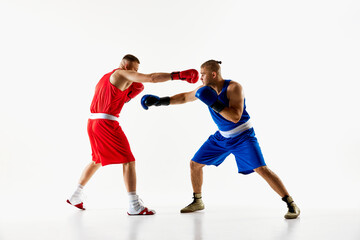 Boxing battle captured between two fighters, boxer in red uniform throwing punch at opponent in blue attire against white studio background. Concept of professional combat sport, competition. Ad
