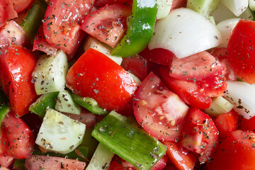 Close-up of a fresh vegetable salad with tomatoes, green bell peppers, and onions, seasoned with herbs and olive oil shows the textures of the freshness and healthiness of the ingredients.