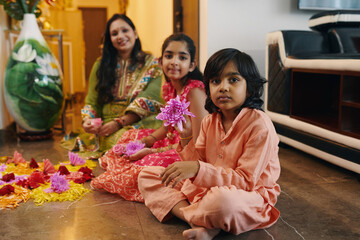 Portrait of Indian children making composition from flowers on the floor together with mother