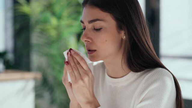 Video of illness business woman sneezing in a tissue while working with computer in a modern office