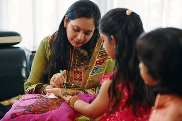 Indian mom drawing pattern from henna to her children at home