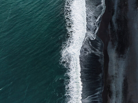 Stunning aerial view of a black sand beach in Iceland, where white foamy waves crash against the shore, creating a striking visual contrast. - Powered by Adobe