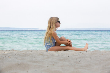Adorable little girl in blue swimwear and black sunglasses on the sand beach