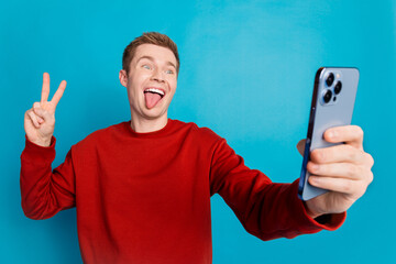 Photo of nice young man selfie v-sign show tongue wear pullover isolated on blue color background