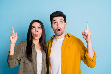 Portrait of two young people look direct fingers up empty space wear shirt isolated on blue color...