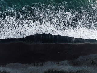 Dramatic contrast of white ocean waves crashing against the black sand beach in Iceland. Captured from above, showcasing the unique natural beauty.