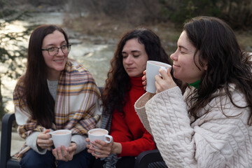 Three Friends Enjoying Hot Beverages by a River