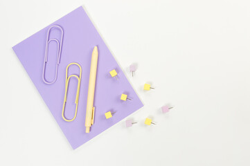 Top view of purple notebook on white background. Paperclips, pen and pins. School, office wallpaper. Flat lay, copy space.
