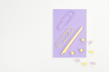 Top view of purple notebook on white background. Paperclips, pen and pins. School, office wallpaper. Flat lay, copy space.