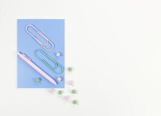 Top view of blue notebook on white background. Paperclips, pen and pins. School, office wallpaper. Flat lay, copy space.