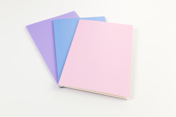 Top view of pink, purple and blue notebooks on white background. School, office wallpaper. Flat lay, copy space.