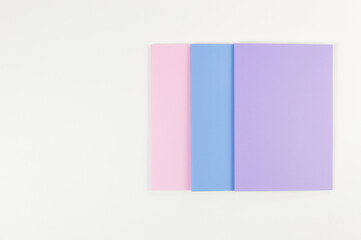 Top view of pink, purple and blue notebooks on white background. School, office wallpaper. Flat lay, copy space.