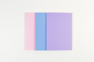 Fototapeta premium Top view of pink, purple and blue notebooks on white background. School, office wallpaper. Flat lay, copy space.