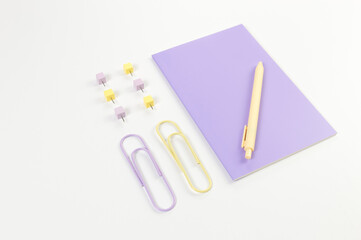 Top view of purple notebook on white background. Paperclips, pen and pins. School, office wallpaper. Flat lay, copy space.