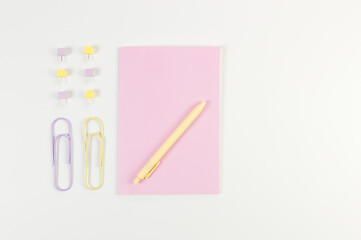 Top view of pink notebook on white background. Paperclips, pen and pins. School, office wallpaper. Flat lay, copy space.